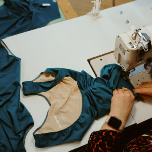 Hands working with a sewing machine to create a leotard with another leotard on the table just to the left of the one being worked on