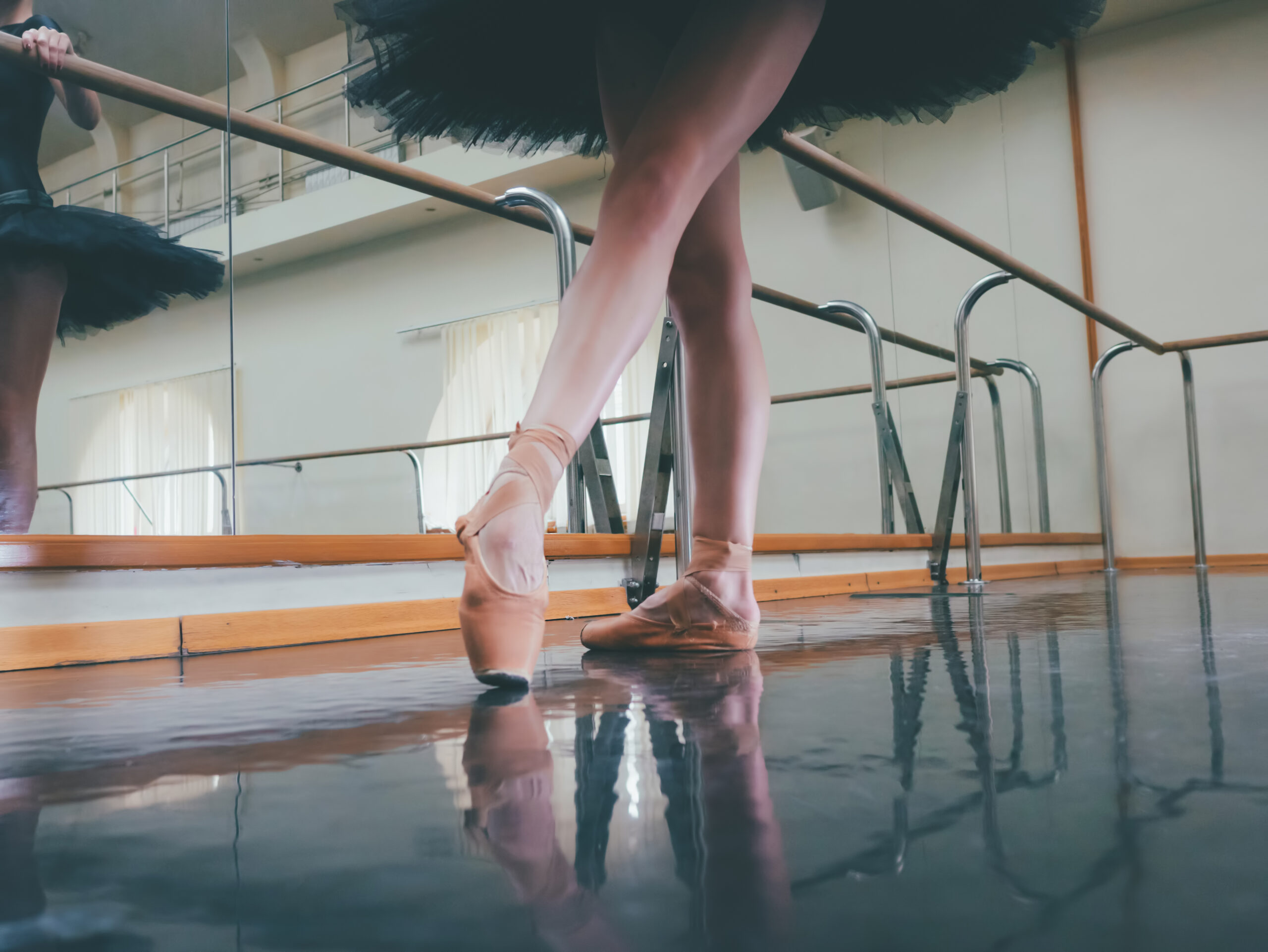 Ballerina dancer in ballet pointe shoes stretches on barre. Woman practicing in studio tutu
