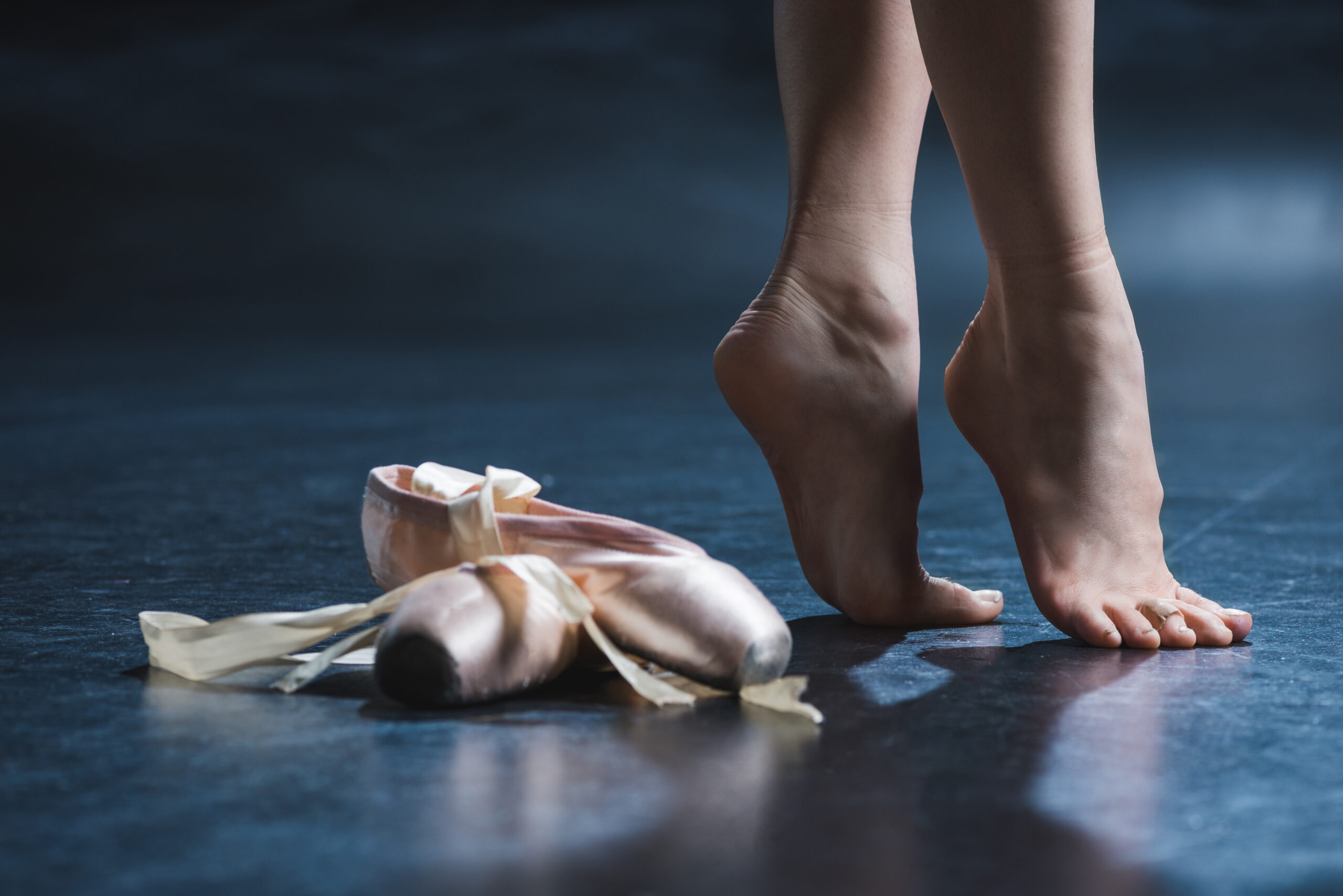 cropped view elegant barefoot ballerina and pointe shoes in dark studio