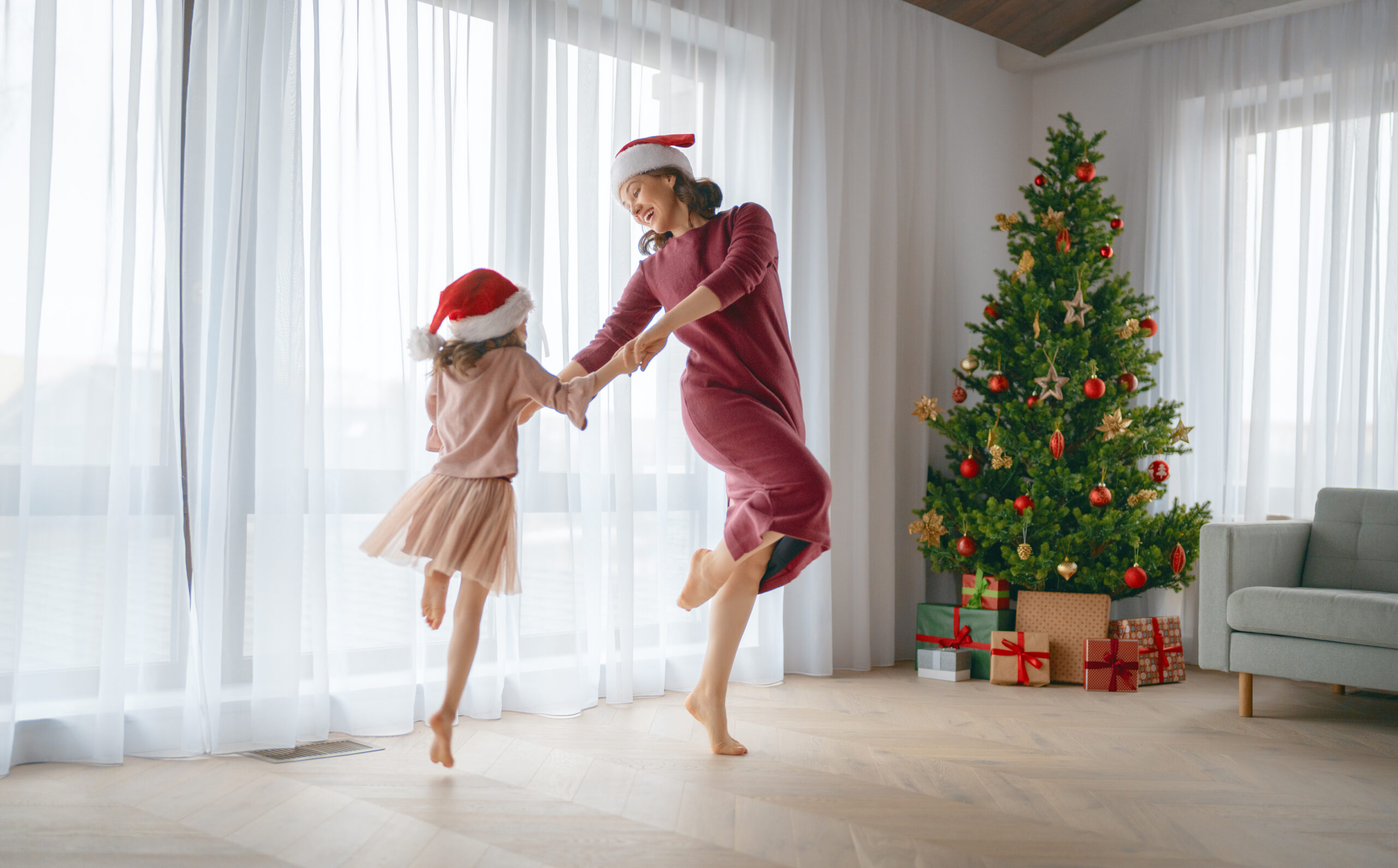Merry Christmas, Happy Holidays. Cheerful mom and her cute daughter girl are dancing. Parent and little child having fun near tree indoors.\ family celebrating Christmas