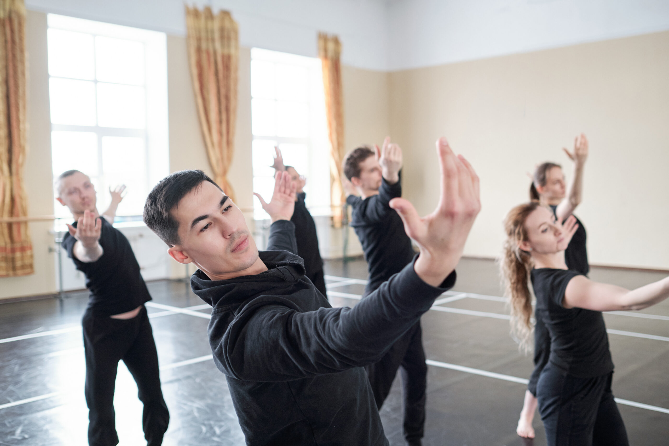 Young handsome man with outstretched arms doing one of dance exercises on background of his classmates in studio